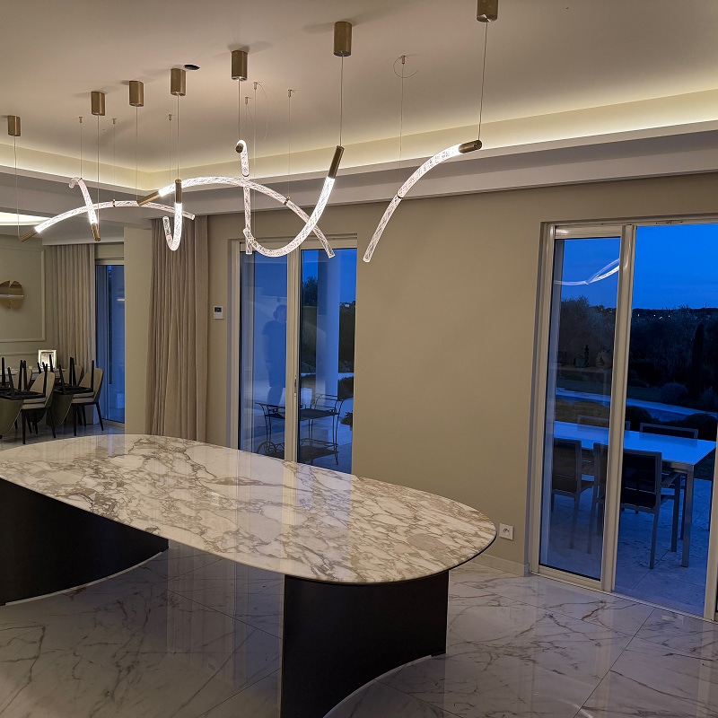 Grand îlot en marbre blanc dans une cuisine moderne de luxe. Luminaire design suspendu composé de tubes de verre incurvés.