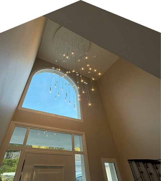 Lustre cascade moderne pour entrée à haut plafond. Entrée double hauteur. Lustre moderne à cascade lumineuse devant une grande fenêtre cintrée. Haut plafond beige.