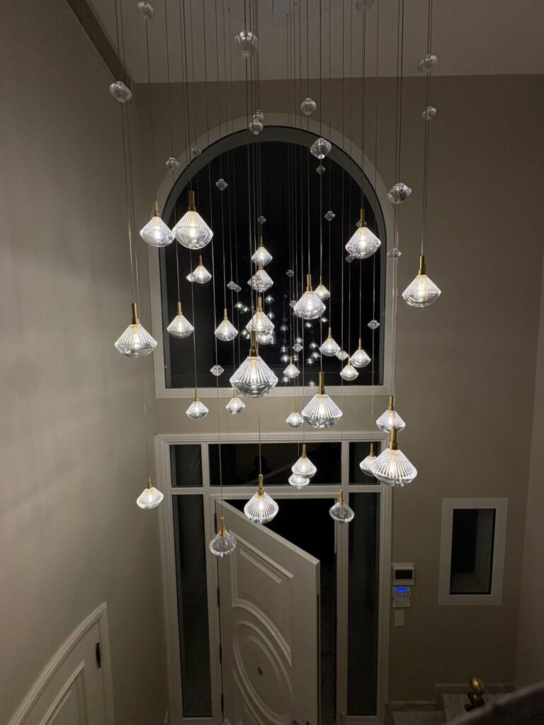 Lustre moderne à multiples suspensions en verre dans une entrée élégante avec une grande fenêtre cintrée de nuit.